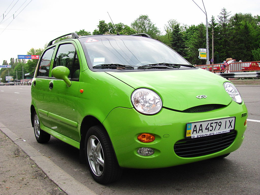 Talvez o carro mais popular da história da Chery, o QQ de cor verde parado em uma avenida.